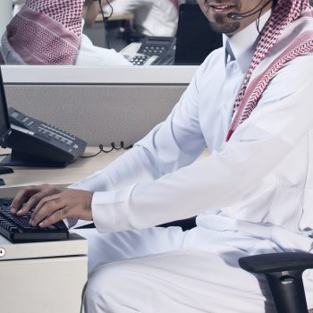 Portrait of a smiling Middle eastern employee with headphones on, in a call center